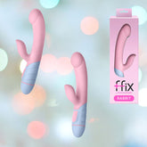 Two Femme Funn FFIX Rabbit Vibrators in pink and pastel blue are depicted alongside their packaging. The packaging features the product image and branding "Femme Funn FFIX Rabbit" in pink and white text. The background is a soft gradient of light blue, green, and pink bokeh.